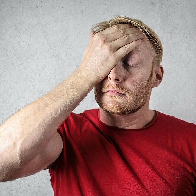 Ein Mann in einem roten T-Shirt bedeckt sein Gesicht mit seiner Hand.
